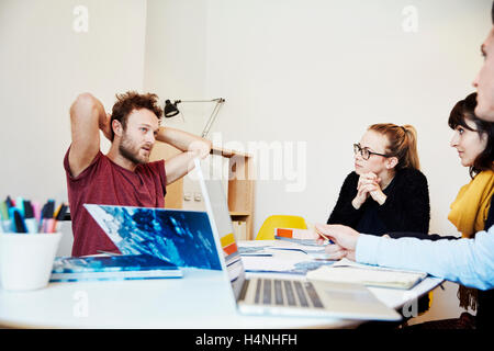 Vier Menschen bei einem Treffen, zwei Männer und zwei Frauen. Laptop Computer, Papier und Noten Bücher auf dem Tisch. Stockfoto