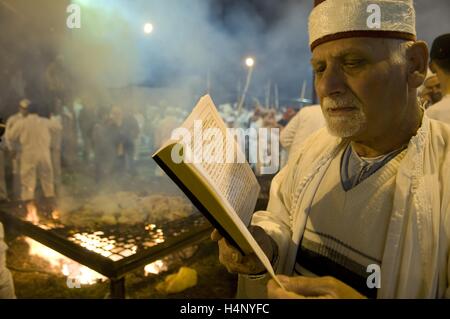 Ein Mitglied der alten Samariter Gemeinschaft lesen ein Gebetbuch in alten hebräischen geschrieben als Samariter um ein Feuer versammeln - Grube, bevor sie Schafe auf Pfählen ins Feuer während der traditionellen Passah schlachten in Kiryat luza Dorf in der Nähe der Stadt Nablus im Westjordanland Israel. Die Samariter, die ihre Wurzeln in der nördlichen West Bank, Beobachten, religiöse Praktiken, die denen des Judentums zu den nördlichen Königreich Israel verfolgen. Stockfoto