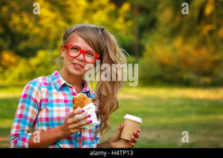 Sehr attraktives Mädchen mit einer Tasse Kaffee und einen Hot Dog in einem Park. Snack. Fast-Food. Stockfoto