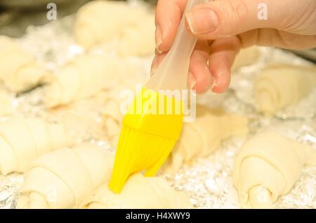 Hausgemachte rohe Croissants mit gelben Pinsel Eier in weiblicher hand Stockfoto