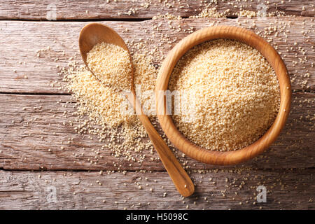 Rohen Couscous in eine hölzerne Schüssel und Löffel auf dem Tisch. Horizontale Ansicht von oben Stockfoto