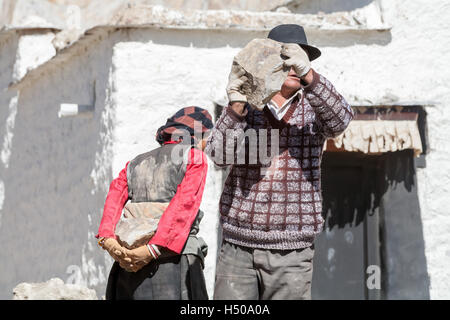 Ein Tibeter entfernt der Tibeterin einen schweren Stein vom Rücken. Old Lhatse, Tibet, China. Stockfoto