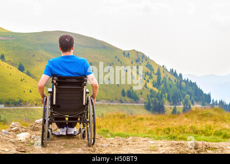 Junger Mann im Rollstuhl an der frischen Luft an einem sonnigen Tag auf dem Berg Stockfoto