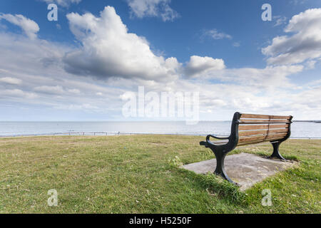 Hölzerne Sitzbänke, Blick auf das Meer unter blauem Himmel mit flauschigen Wolken an einem schönen Sommertag in Northumberland Stockfoto