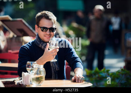 Junger Mann sitzt am Tisch outdoor-Bar mit einem Glas Weißwein ablöschen und auf die Kamera Stockfoto