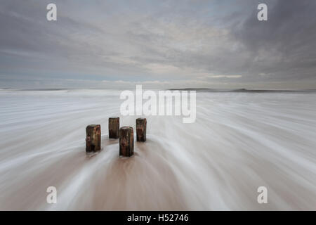 Holzpfosten von einem alten Buhne am Strand als die Nordsee rauscht in bei Flut an der Northumberland Küste an einem grauen Tag Stockfoto