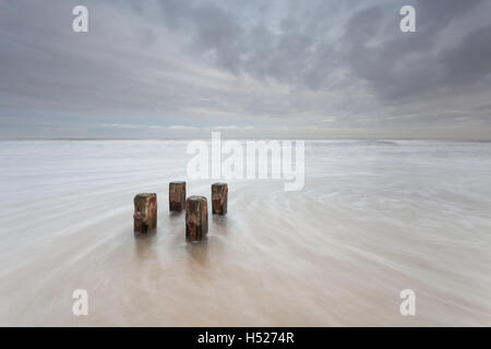 Holzpfosten von einem alten Buhne am Strand als die Nordsee rauscht in bei Flut an der Northumberland Küste an einem grauen Tag Stockfoto