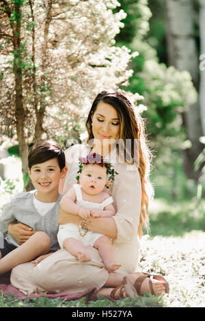 Porträt von ein lächelndes Baby, Mutter und junge Mädchen mit einem Blumen-Kranz auf dem Kopf, sitzt in einem Garten. Stockfoto