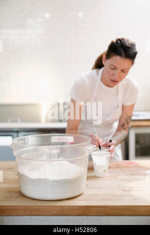 Frau trägt eine weiße Schürze an einem Schalter der Arbeit in einer Bäckerei Mehl zu messen. Stockfoto