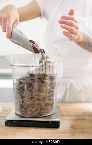 Nahaufnahme einer Frau trägt eine weiße Schürze an einem Schalter der Arbeit in einer Bäckerei mit einem Gewicht von Schokolade. Stockfoto