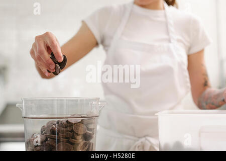 Nahaufnahme einer Frau trägt eine weiße Schürze an einem Schalter der Arbeit in einer Bäckerei mit Schokolade. Stockfoto