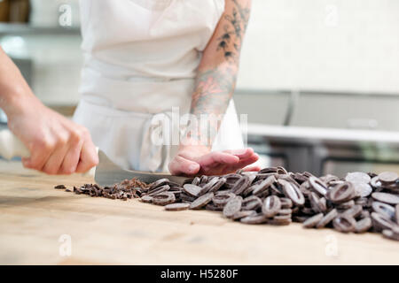 Nahaufnahme einer Frau trägt eine weiße Schürze an einem Schalter der Arbeit in einer Bäckerei Schokolade hacken. Stockfoto