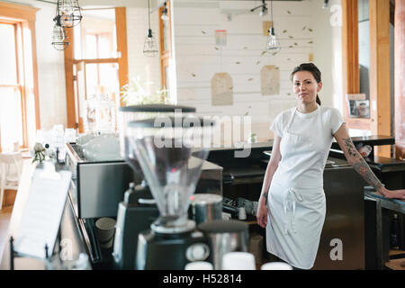 Frau trägt eine weiße Schürze in einem Café in die Kamera Lächeln. Stockfoto