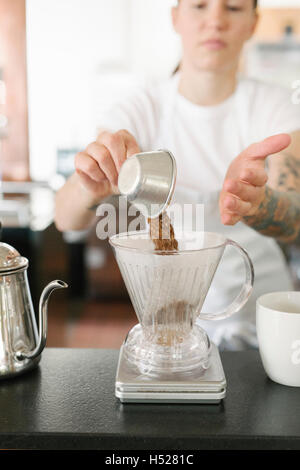 Frau trägt eine weiße Schürze in einem Coffee-Shop, Filterkaffee machen. Stockfoto