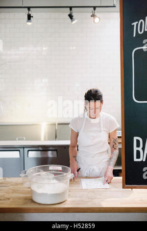 Frau trägt eine weiße Schürze an einem Schalter der Arbeit in einer Bäckerei. Stockfoto