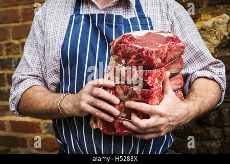 Metzger in blau gestreiften Schürze halten ein großes Stück Rindfleisch. Stockfoto
