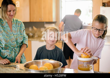 Familie, die Zubereitung des Frühstücks in der Küche, Mädchen, die Orangen auspressen. Stockfoto