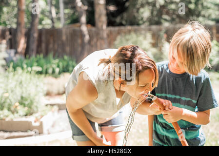 Mutter und Sohn in einem Garten, Trinkwasser aus einem Gartenschlauch. Stockfoto