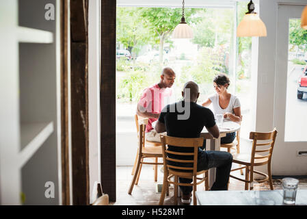 Zwei Männer und eine Frau sitzen an einem Tisch in einem Café zu Mittag. Stockfoto