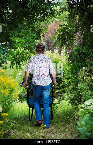 Eine Frau, die Schubkarre von Garten Clippings entlang eines Pfades. Stockfoto