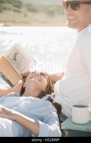 Mann und Frau auf einem Steg liegend ein Buch lesen. Stockfoto