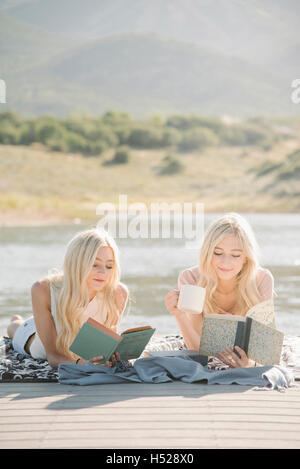 Zwei blonde Schwestern liegen auf einem Steg, ein Buch zu lesen. Stockfoto