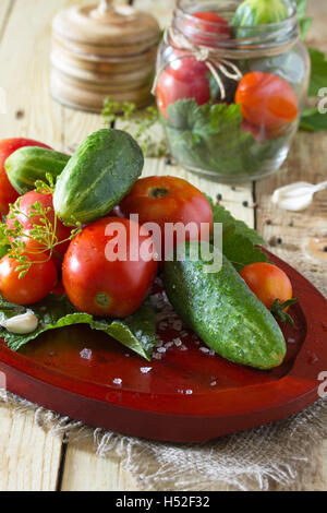Erhaltung der frische und eingelegte Gurken und Tomaten, Gewürze und Knoblauch auf einem Holztisch. Haus Gemüsekonserven. Stockfoto