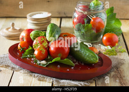 Erhaltung der frische und eingelegte Gurken und Tomaten, Gewürze und Knoblauch auf einem Holztisch. Haus Gemüsekonserven. Stockfoto
