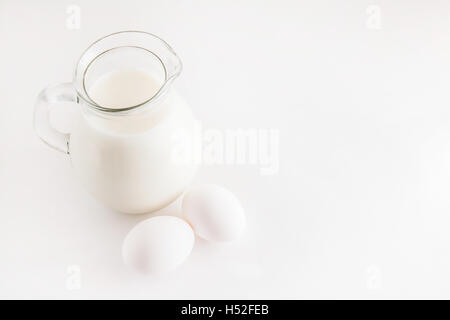 Krug mit Milch und zwei weiße Hühnereier auf weißem Hintergrund. Stockfoto