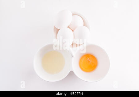 Huhn von rohem Eiweiß und Eigelb getrennt und ganze Eiern in einer Schüssel isoliert auf weiss Stockfoto