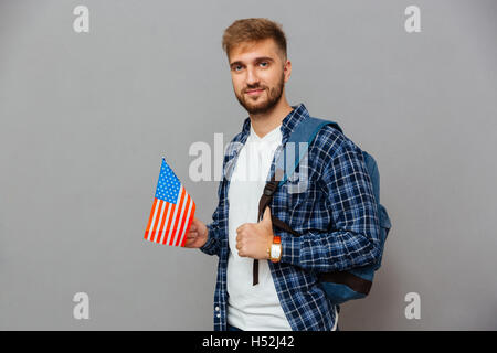 Porträt eines bärtigen Mannes mit Rucksack und USA Flagge auf einem grauen Hintergrund isoliert Stockfoto