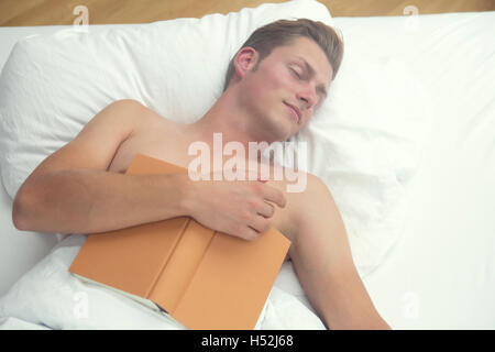 hübscher blonder Mann schlafend im Bett und ein Buch hält Stockfoto
