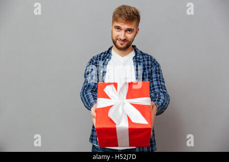 Porträt eines glücklichen bärtigen Mannes, Geschenk-Box vor der Kamera über grauen Hintergrund Stockfoto