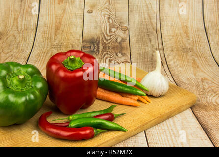 Zwei große, süße Paprika, vier Chili, Karotten und Knoblauch auf eine Arbeitsplatte und einem alten Holztisch angeordnet. Horizontale Ansicht. Stockfoto