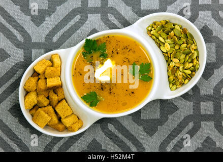 Schließen Sie die Ansicht auf weiße Schüssel mit Kürbissuppe, Kürbiskerne und kleinen, gebackenen Croutons Brot, die frischen Blätter des Parsl vorbereitet Stockfoto