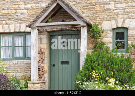 Englischen alten Steinhaus mit grünen Türen, hölzernen Eingang Baldachin und Kräuter, bunte Blumen im Vorgarten gepflanzt Stockfoto