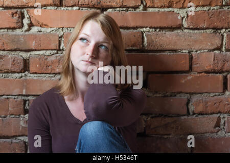 Porträt von Ernst langhaarige junge Frau sitzt vor der Wand. Frau freut sich auf das natürliche Licht. Stockfoto