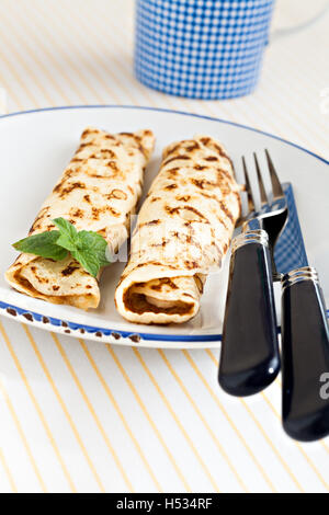 dünne Pfannkuchen gerollt Crepes Minze auf einem Teller mit Messer und Gabel. Stockfoto