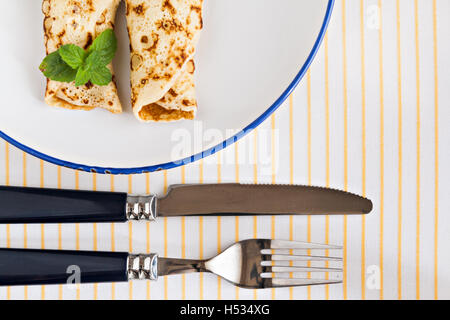 dünne Pfannkuchen gerollt Crepes Minze auf einem Teller mit Messer und Gabel. Stockfoto