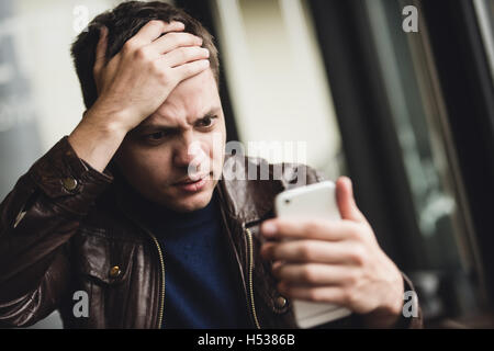 Schlechte Nachrichten. Deprimiert junger Mann, mit dem Ausdruck ihrer Negativität, beim Lesen der Nachricht auf dem Handy Stockfoto