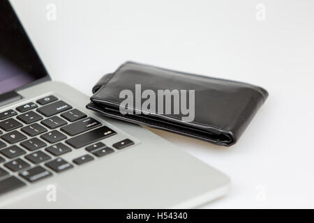 schwarze Leder-Portemonnaie neben einem Laptop auf dem Schreibtisch liegen. Studio gedreht auf weißem Hintergrund Stockfoto