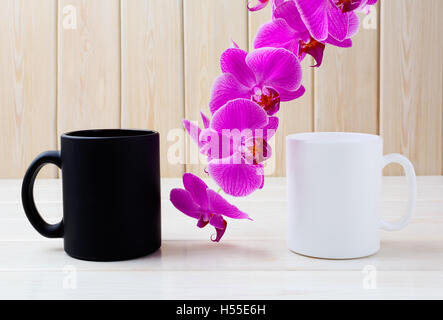Weiße und schwarze Becher Mockup mit rosa Orchidee. Kaffee-Obertasse Mock-up. Leere Becher Mockup zur Produktpräsentation.  Zwei Kaffeetassen. Stockfoto
