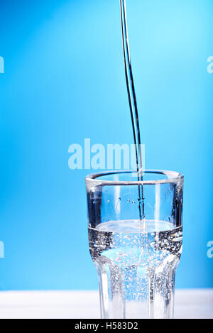 Gießen Wasser mit Spashes im Glas auf einem blauen Hintergrund