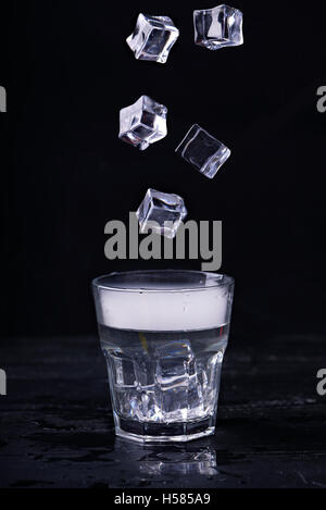 Heißes Wasser mit viel Dampf in ein Glas und Eiswürfeln in Bewegung auf einem schwarzen Hintergrund. Dunkles Foto. Konzept-Foto: drei staatliche o