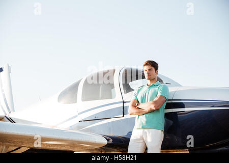 Zuversichtlich junger Mann mit verschränkten vor kleinen Flugzeug Stockfoto