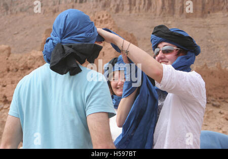 Touristen aus dem Westen anpassen ihrer traditionellen marokkanischen Shesh Kopfschmuck vor Einschiffung auf einem Kamelritt in die Wüste Sahara Stockfoto