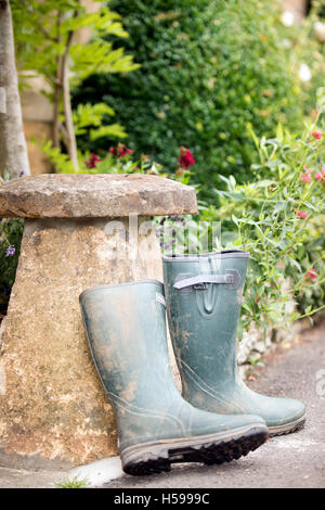 Ein paar Gummistiefel lehnte sich gegen einen Staddle Stein außerhalb einer Berghütte Cotswold, UK Stockfoto