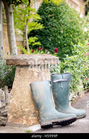 Ein paar Gummistiefel lehnte sich gegen einen Staddle Stein außerhalb einer Berghütte Cotswold, UK Stockfoto