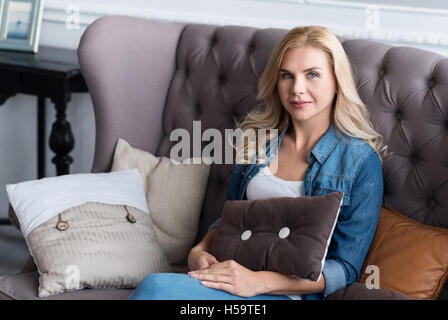 Hübsche blonde Frau sitzt auf graue couch Stockfoto