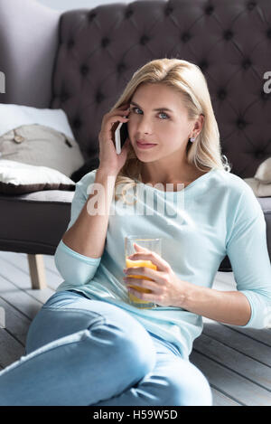 Blonde Dame Saft Glas halten und im Gespräch per Telefon Stockfoto